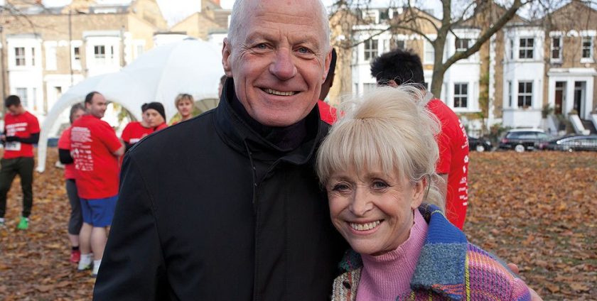 An older man and woman pose and smile together outside at a running event